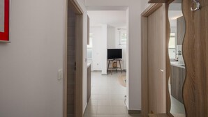 Un couloir mène à un espace de vie comprenant un téléviseur, une petite table et une chaise.