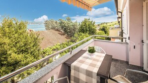 Un balcon avec une nappe à carreaux, un pot de fleurs et une vue sur la mer et la verdure.