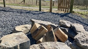 Un espace recouvert de gravier, avec une pile de bois de chauffage et, au fond, une porte en bois.
