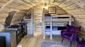 Une chambre mansardée chaleureuse, avec un lit superposé, un petit coin cuisine, un fauteuil violet et un tapis à motifs.