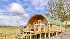Une cabane en bois avec un toit vert, une véranda et une petite table accompagnée de sa chaise.