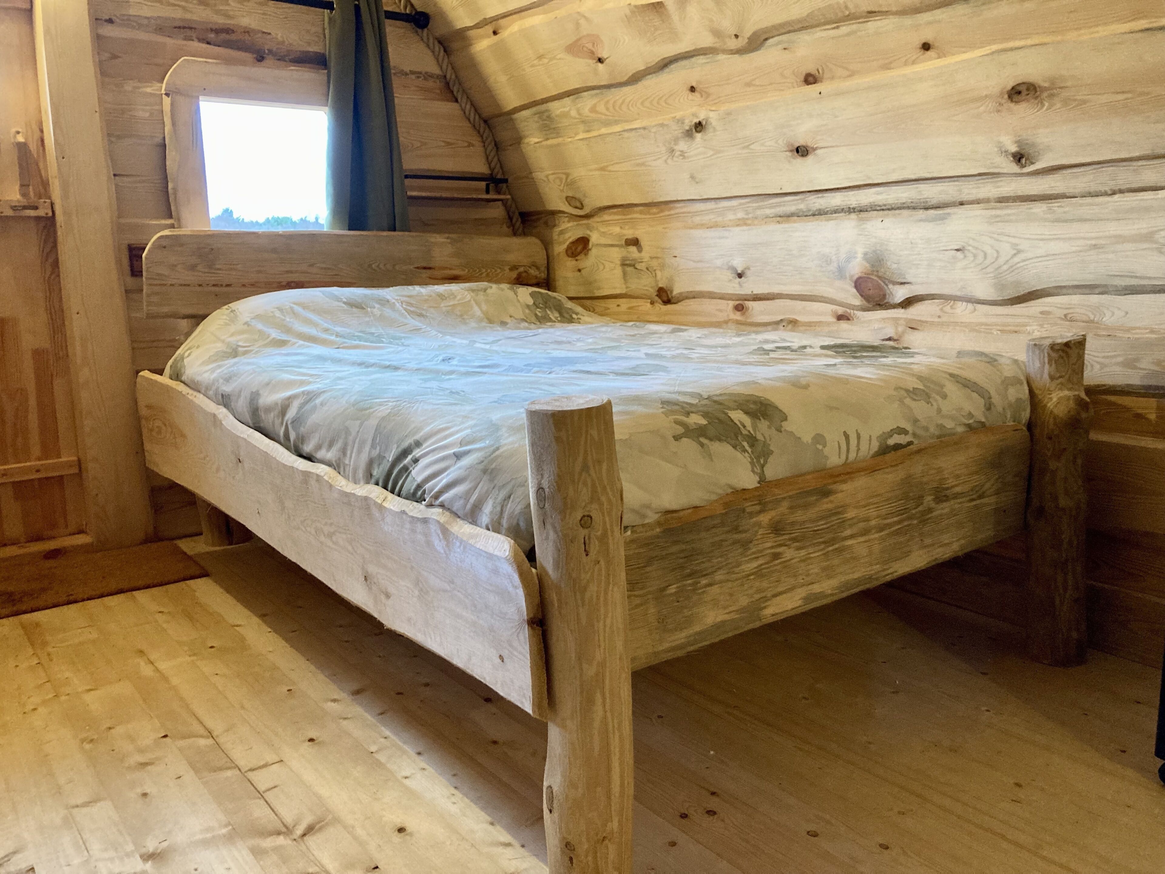 A wooden bed in a cabin-style room with a sloped ceiling and a window.