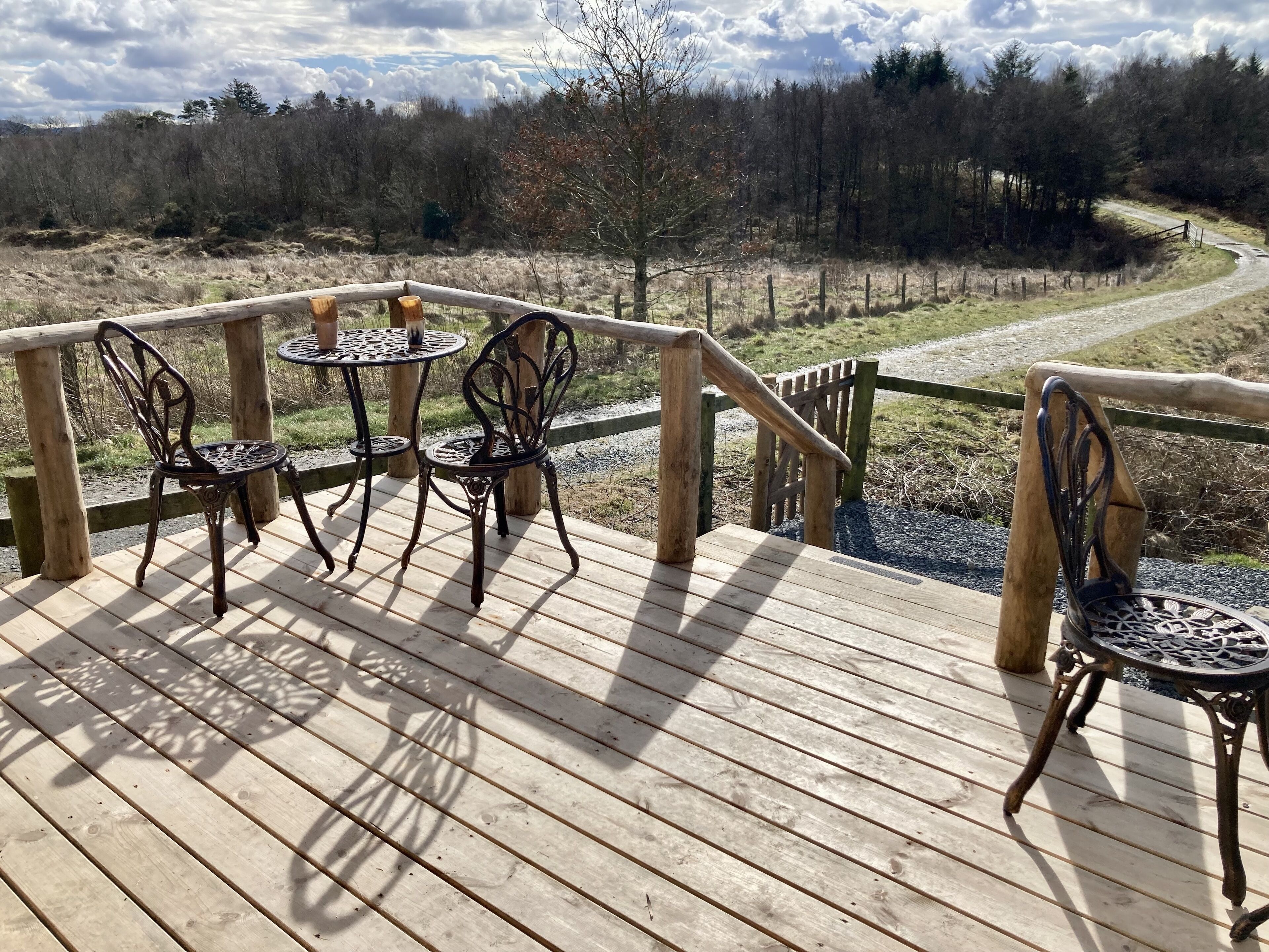 A wooden deck with two metal tables and chairs, overlooking a forested area.