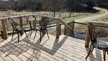 A wooden deck with two metal tables and chairs, overlooking a forested area.