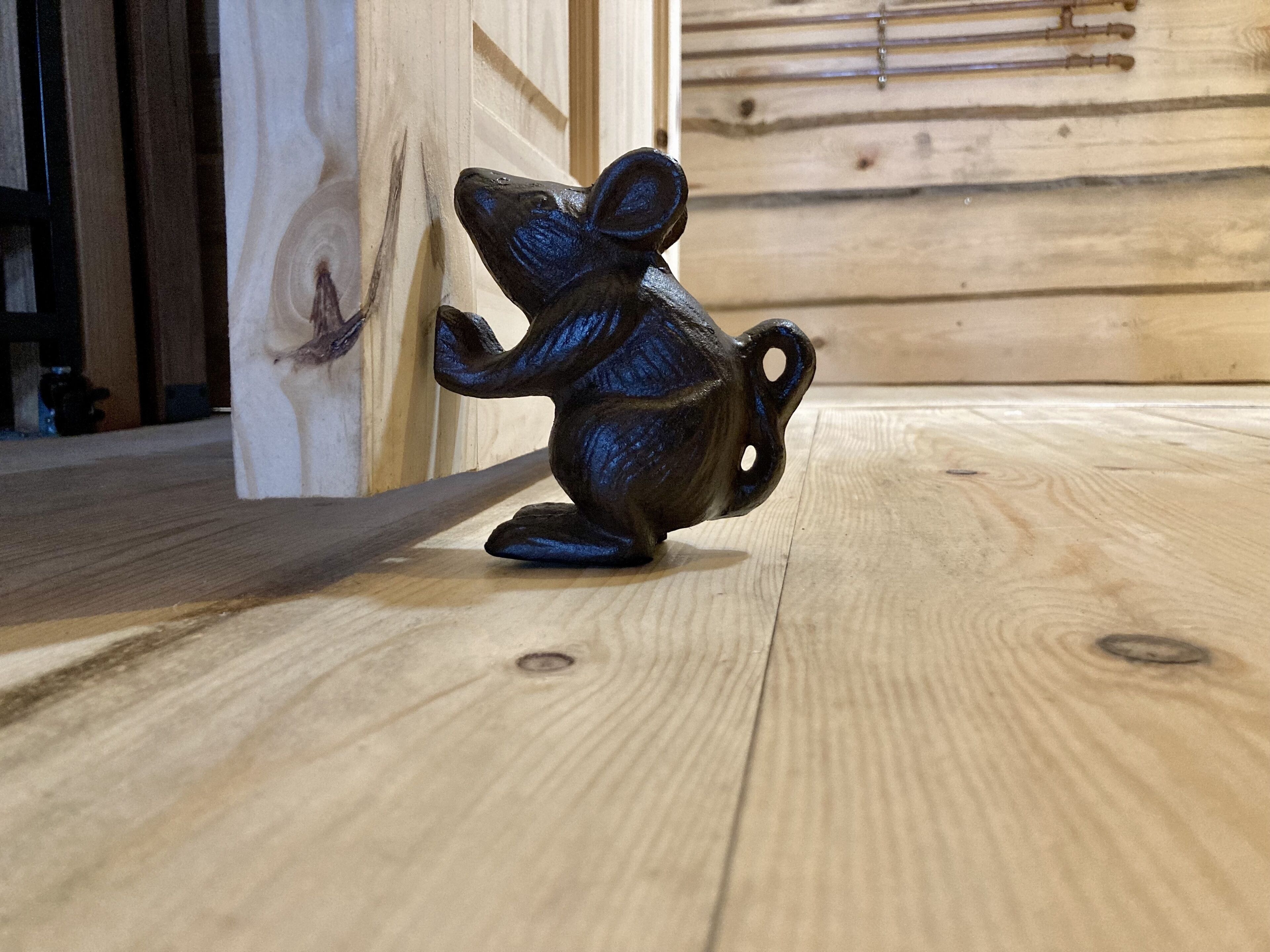 Een klein, donker beeldje van een muis op een houten vloer.