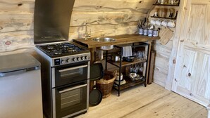 Une cuisine compacte équipée d’une cuisinière à gaz, d’un four et d’une étagère en bois où sont rangés les ustensiles de cuisine.