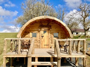 A wooden cabin with a porch, two windows, and a door. - The Prancing Moose (Ystrad Meurig)