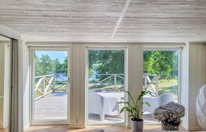 Een kamer met grote schuifdeuren die uitkomen op een terras met houten balustrade en uitzicht op een meer en bomen.