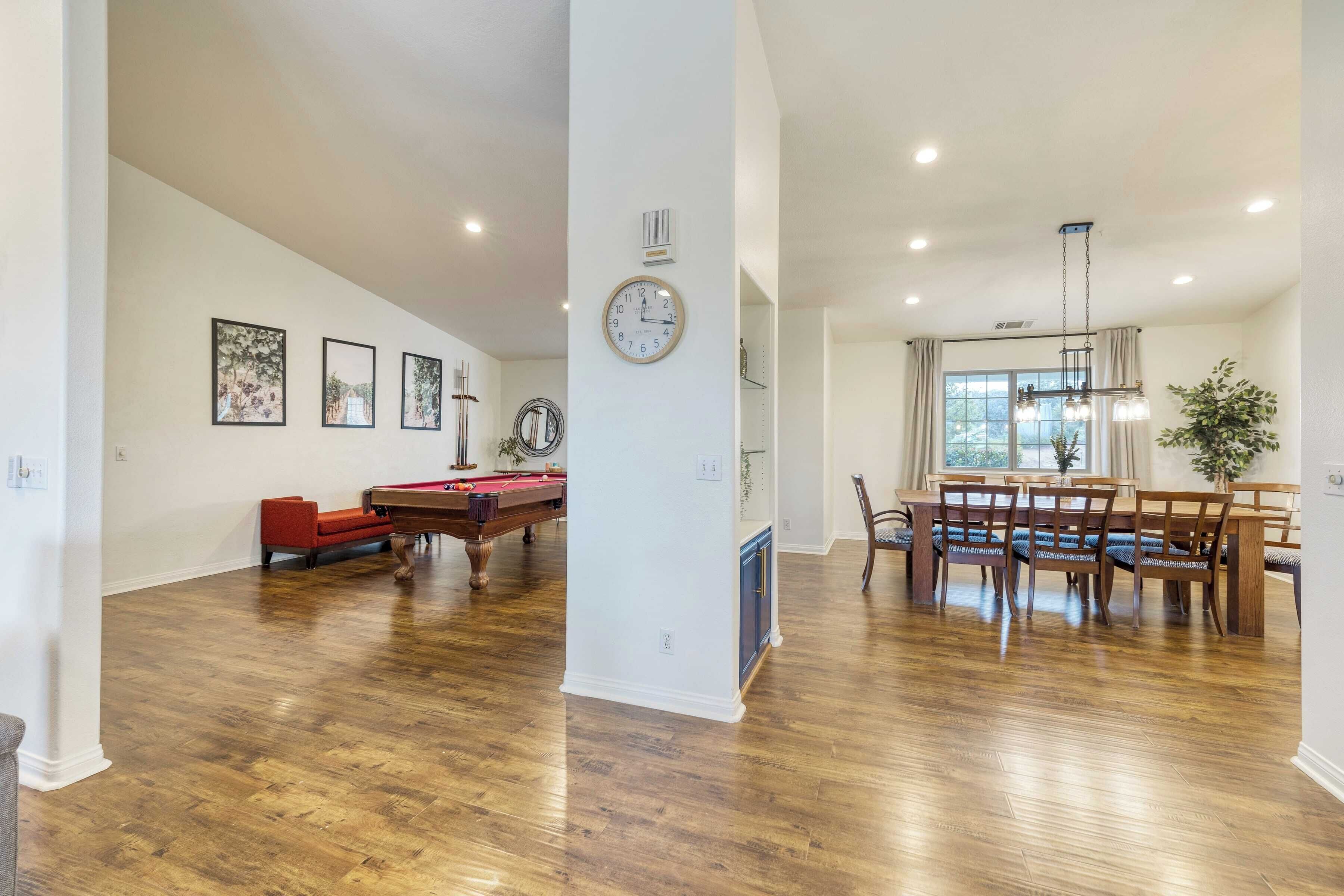 A spacious living room with a pool table, red sofa, and a dining area with wooden chairs and a chandelier.