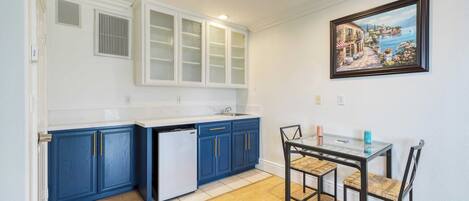 A kitchen with blue cabinets, a white dishwasher, and a dining table with chairs.