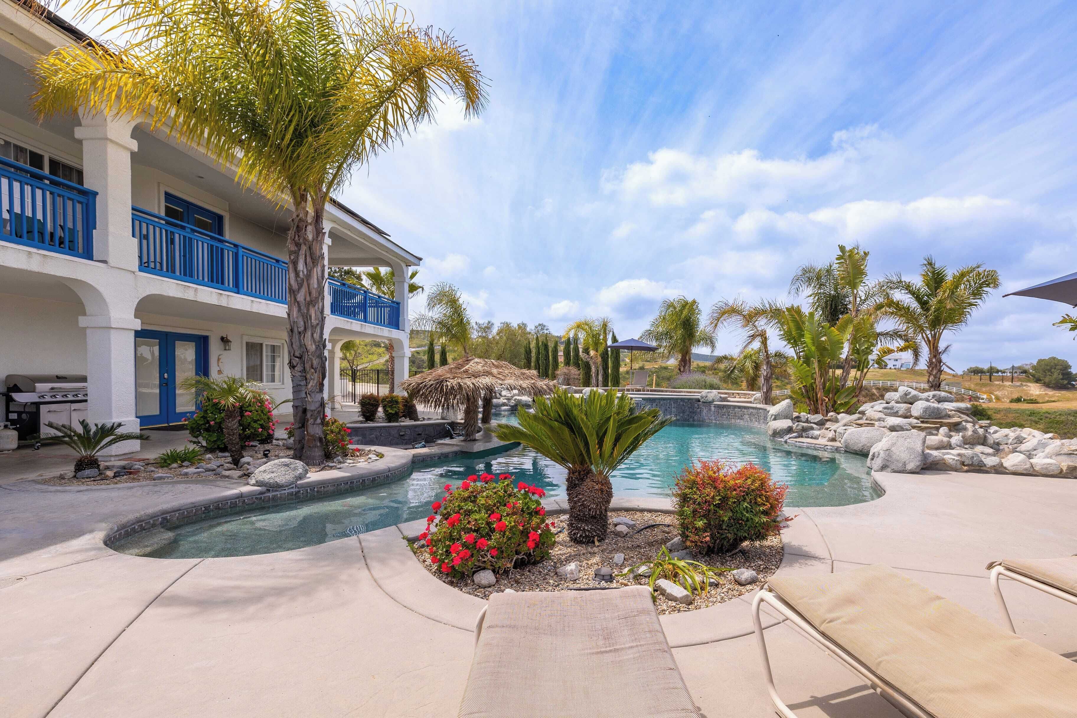 A pool area with lounge chairs, a palm tree, and a building with blue railings.