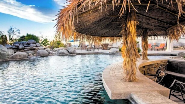 A pool area with a thatched roof structure, stone seating, and a view of the surrounding landscape. - 5-acre Hilltop Estate w/ Resort Pool + Game Room Le Grand Bleu by Avantstay (Temecula)