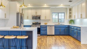 A modern kitchen with white cabinets, blue accents, stainless steel appliances, and wooden bar stools. - 5-acre Hilltop Estate w/ Resort Pool + Game Room Le Grand Bleu by Avantstay (Temecula)