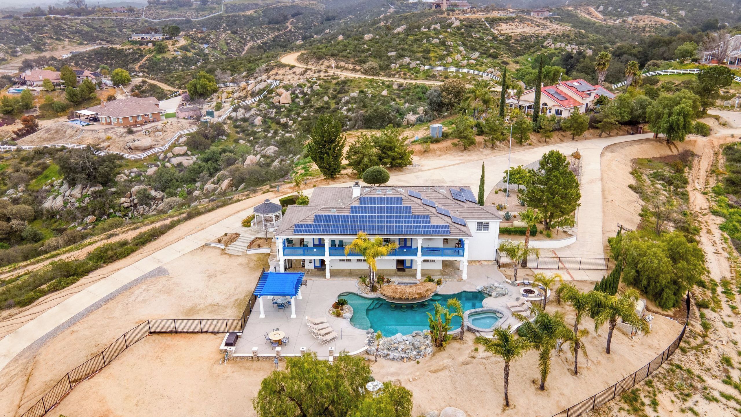Una casa grande con piscina, rodeada por una zona vallada y un paisaje montañoso.