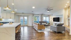 A modern kitchen with a marble countertop, a dining area with a bar stool, a living room with a sofa and a TV, and a balcony with a view. - 5-acre Hilltop Estate w/ Resort Pool + Game Room Le Grand Bleu by Avantstay (Temecula)