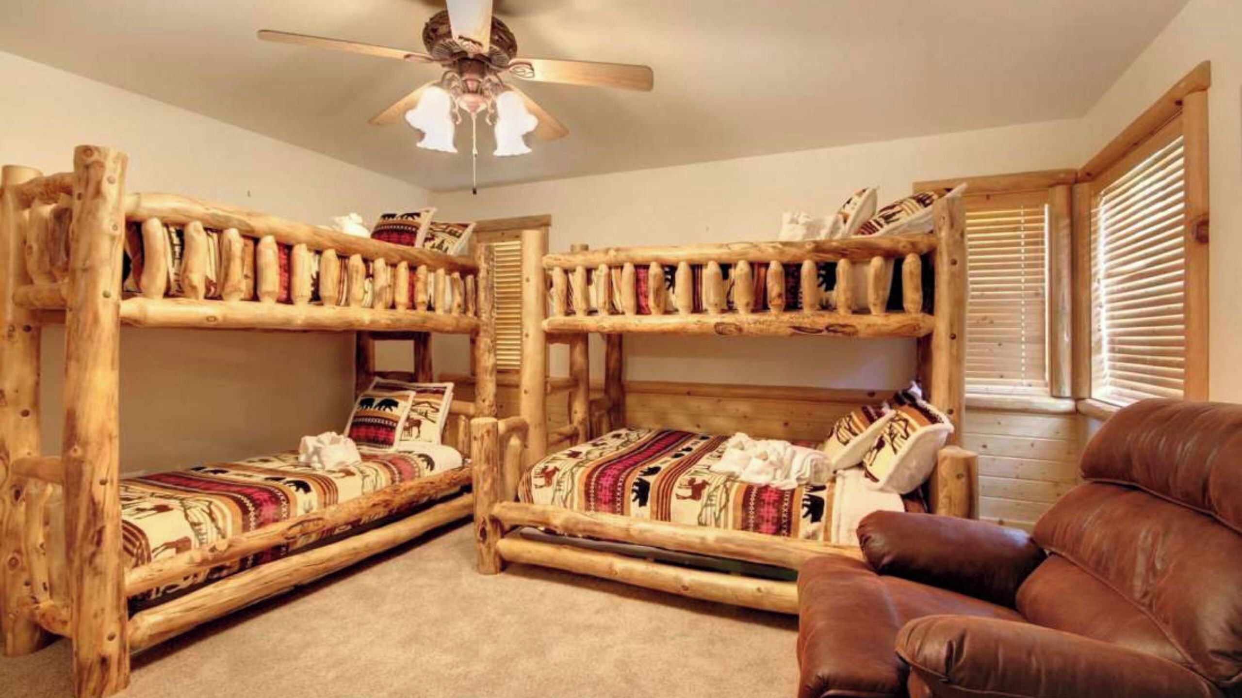 A room with two bunk beds, a ceiling fan, and a leather chair.