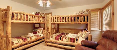 A room with two bunk beds, a ceiling fan, and a leather chair.