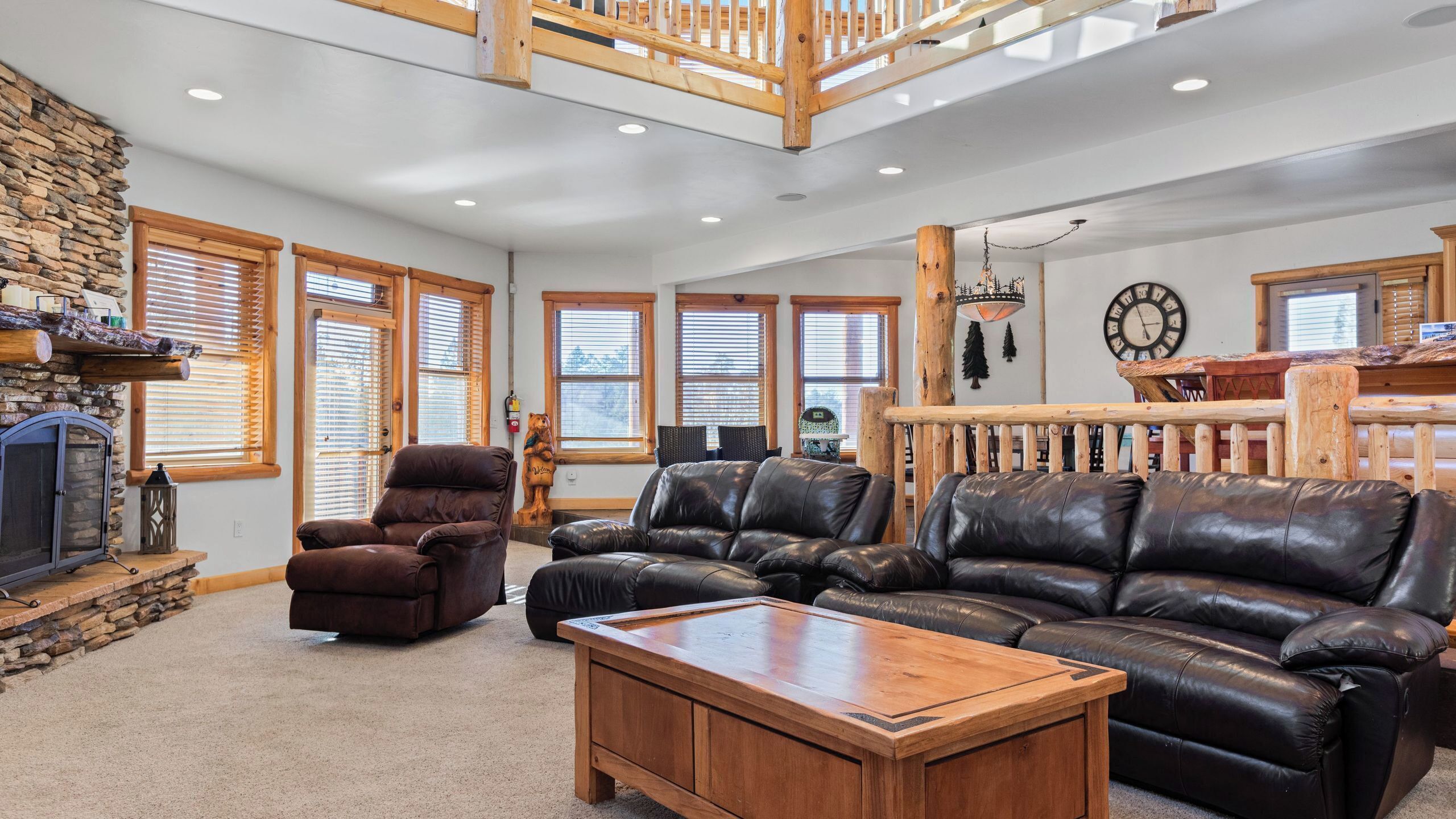 A spacious living room with a stone fireplace, leather sofas, and a wooden coffee table.