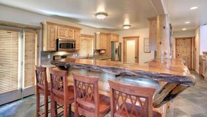Una cocina con armarios de madera, una isla central con taburetes de bar y un refrigerador de acero inoxidable.