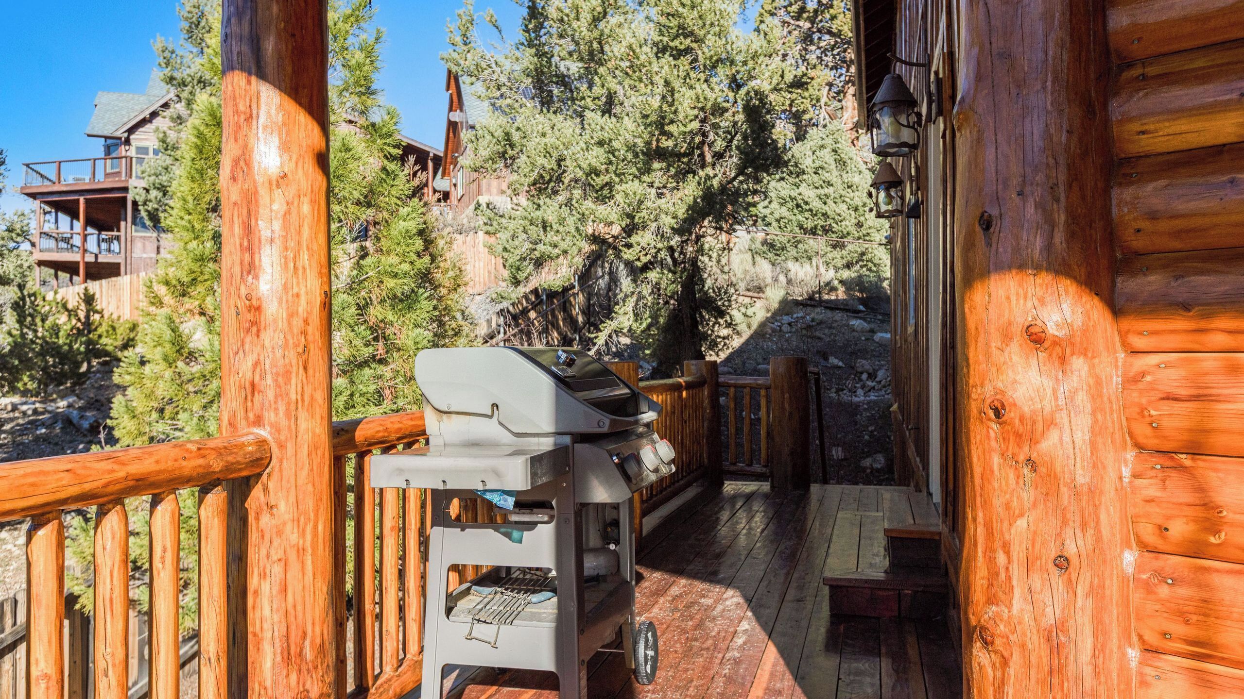 Eine Holzterrasse mit Grill, Holzwerteln und Blick auf eine Bergliege.