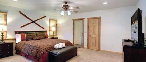 A bedroom with a large bed, a ceiling fan, two doors, a dresser, and a TV.