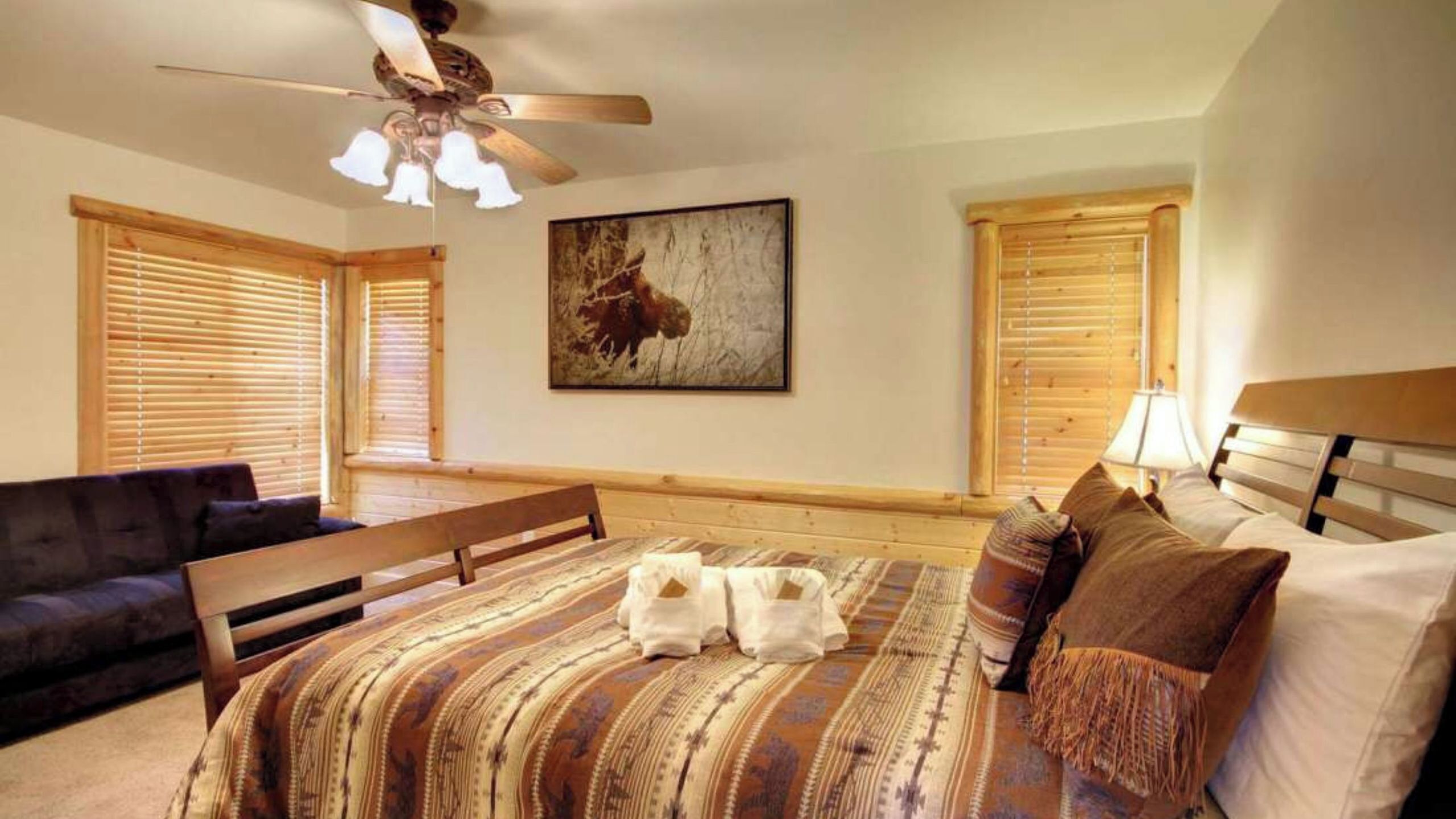A bedroom with a bed, a bench, a ceiling fan, and a painting on the wall.