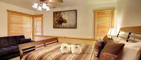 A bedroom with a bed, a bench, a ceiling fan, and a painting on the wall.