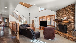 Un amplio salón con chimenea de piedra, sillón de cuero y televisor.