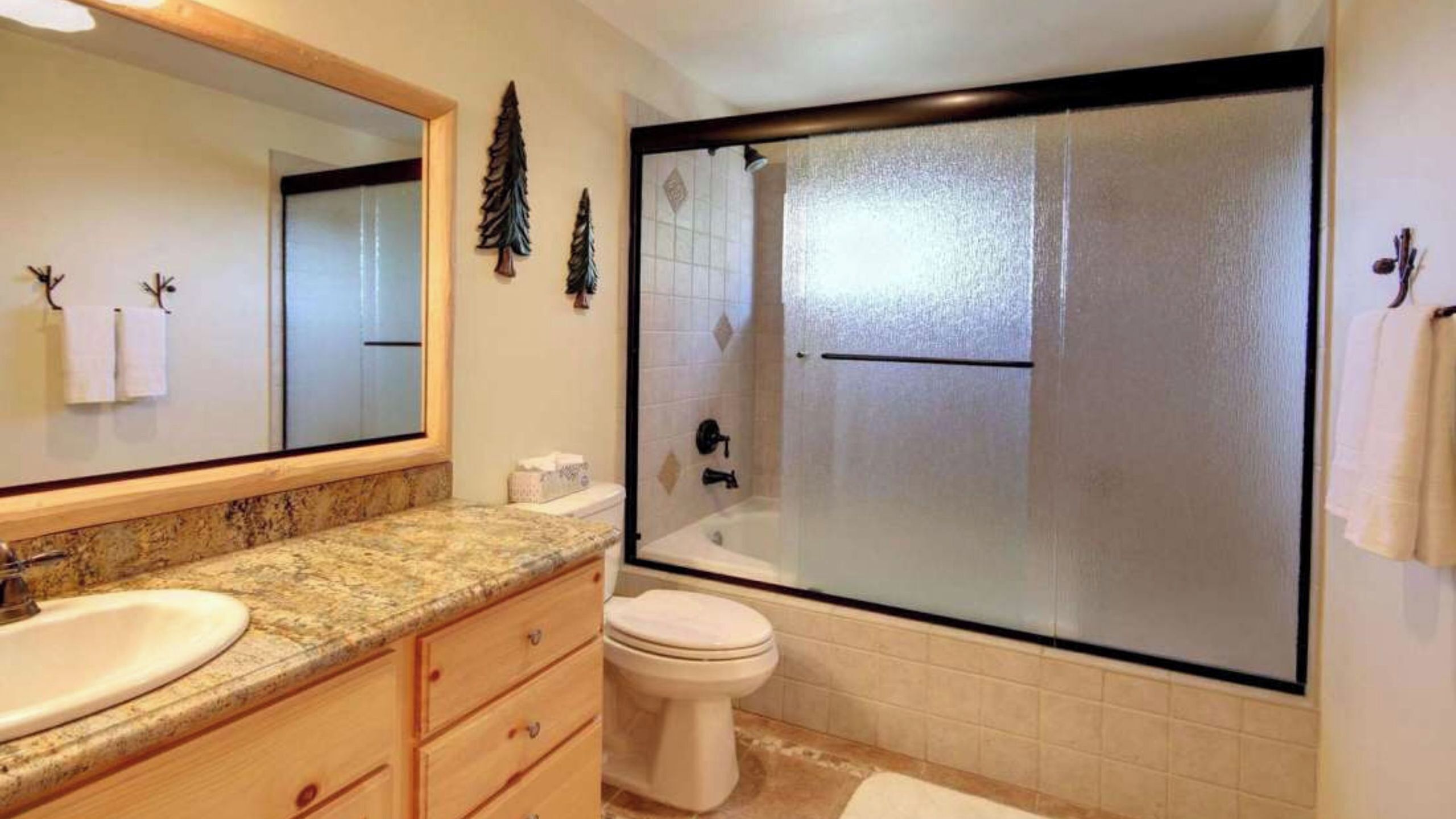 A bathroom with a large mirror, a sink, a toilet, and a glass-enclosed shower.