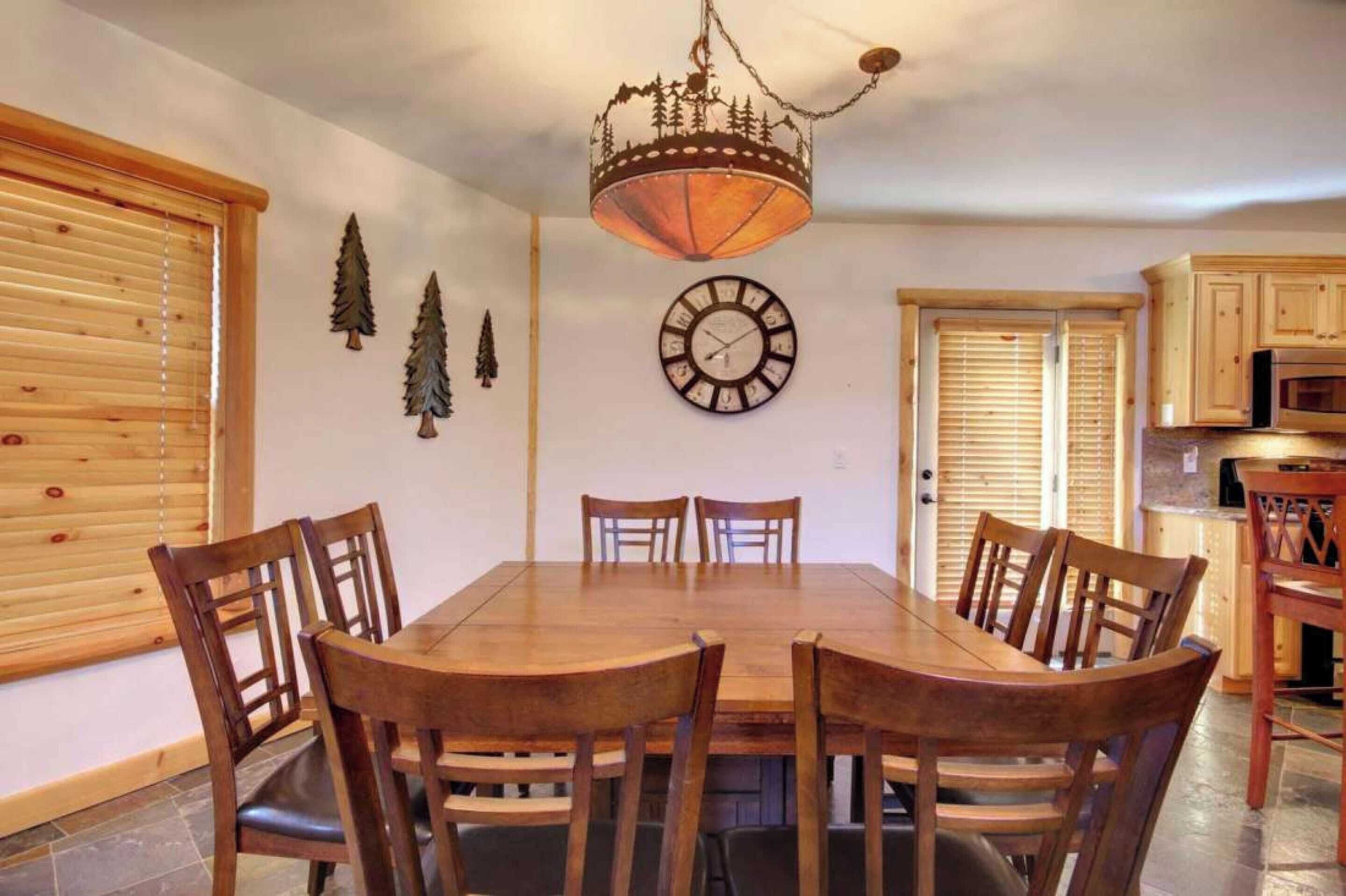 A dining area with a wooden table and chairs, a chandelier, a clock, and wooden cabinets.