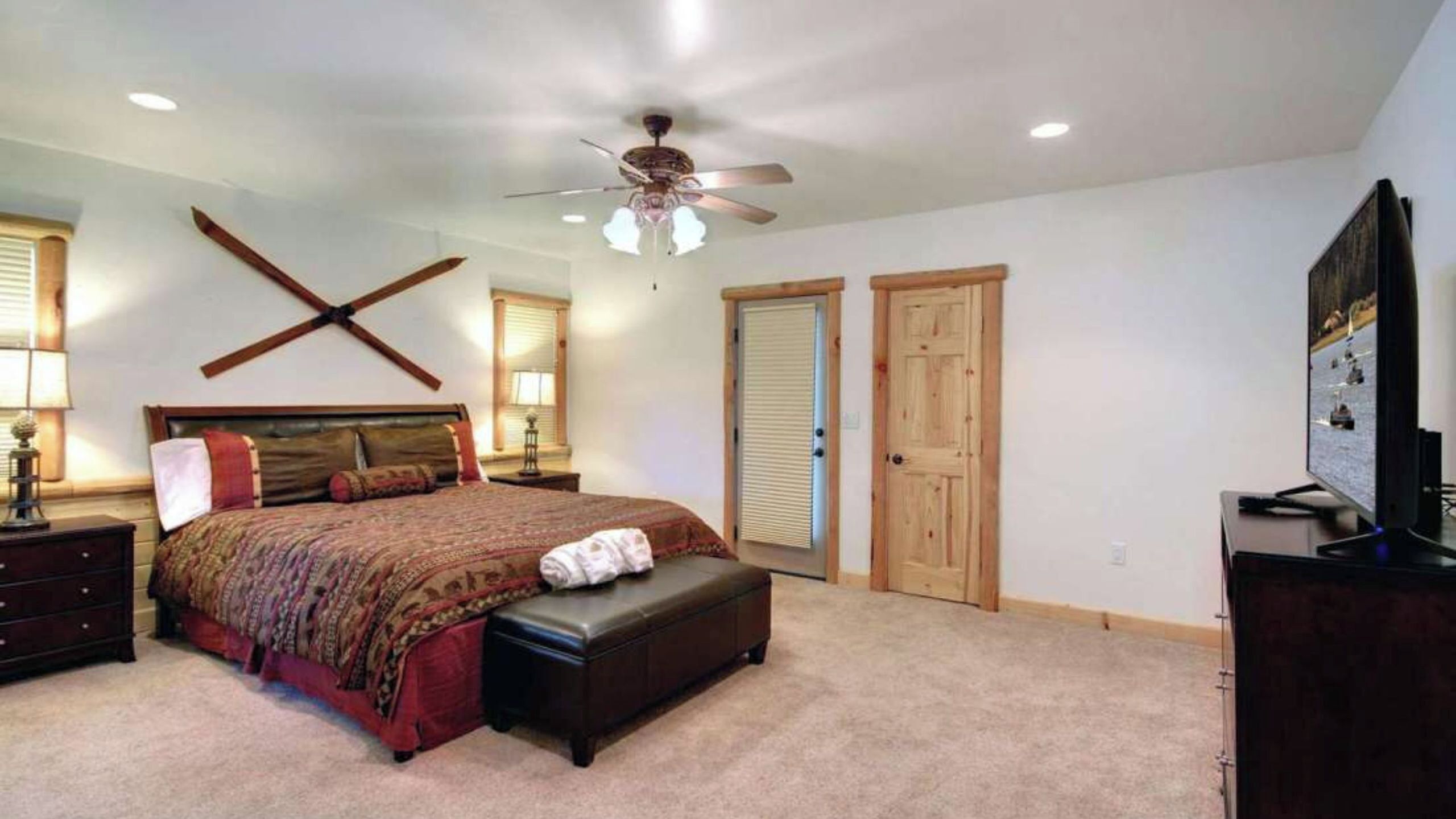 A bedroom with a bed, a ceiling fan, a dresser, and a television.