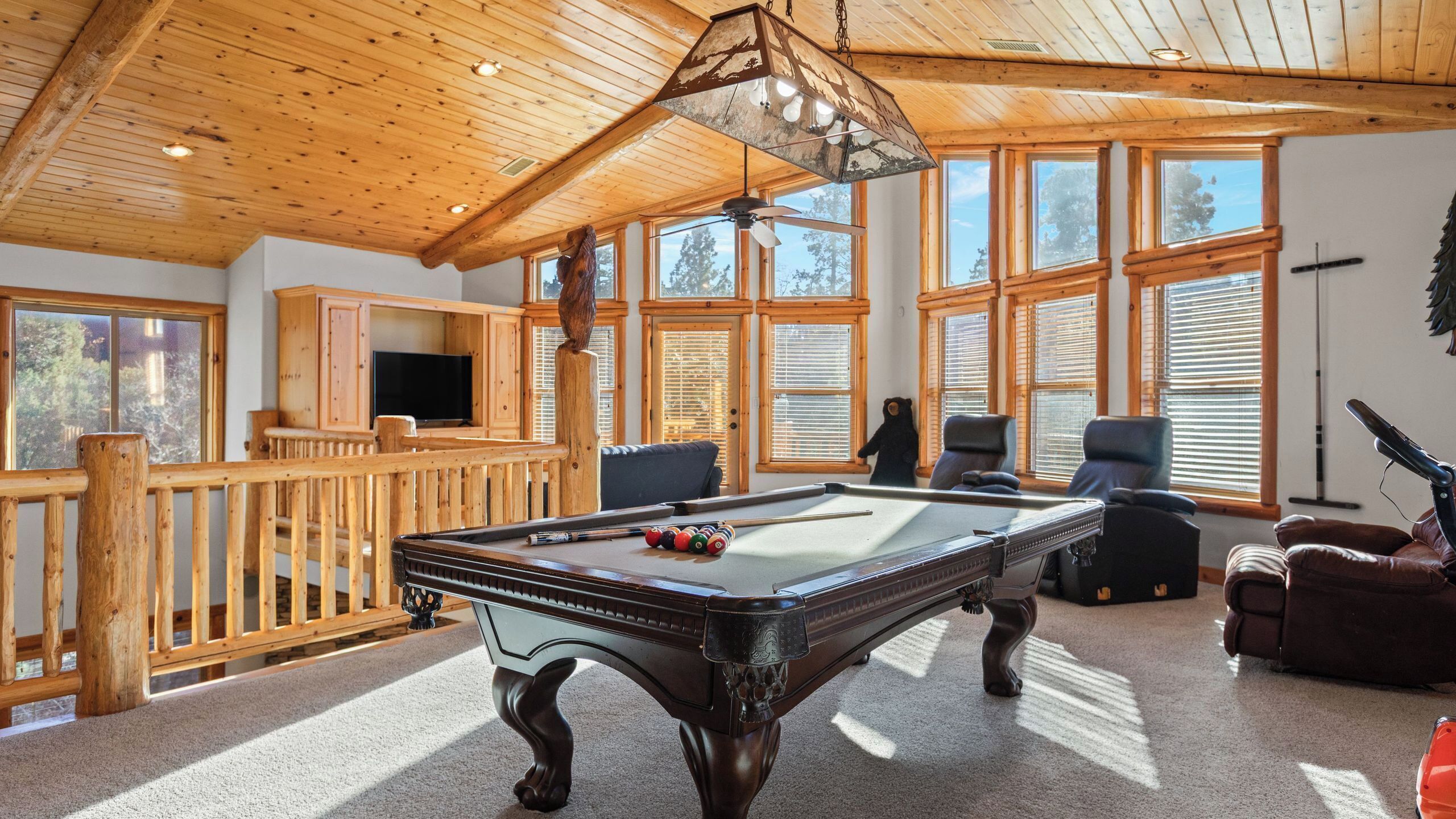A pool table in a room with wooden beams and large windows.