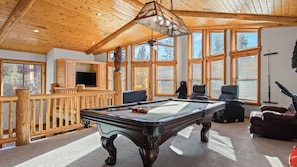 Une table de billard dans une pièce dotée de poutres en bois et de grandes fenêtres.