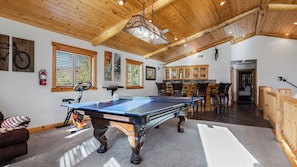 Une table de billard dans une pièce dont le plafond est orné de poutres en bois, avec un extincteur et un vélo.