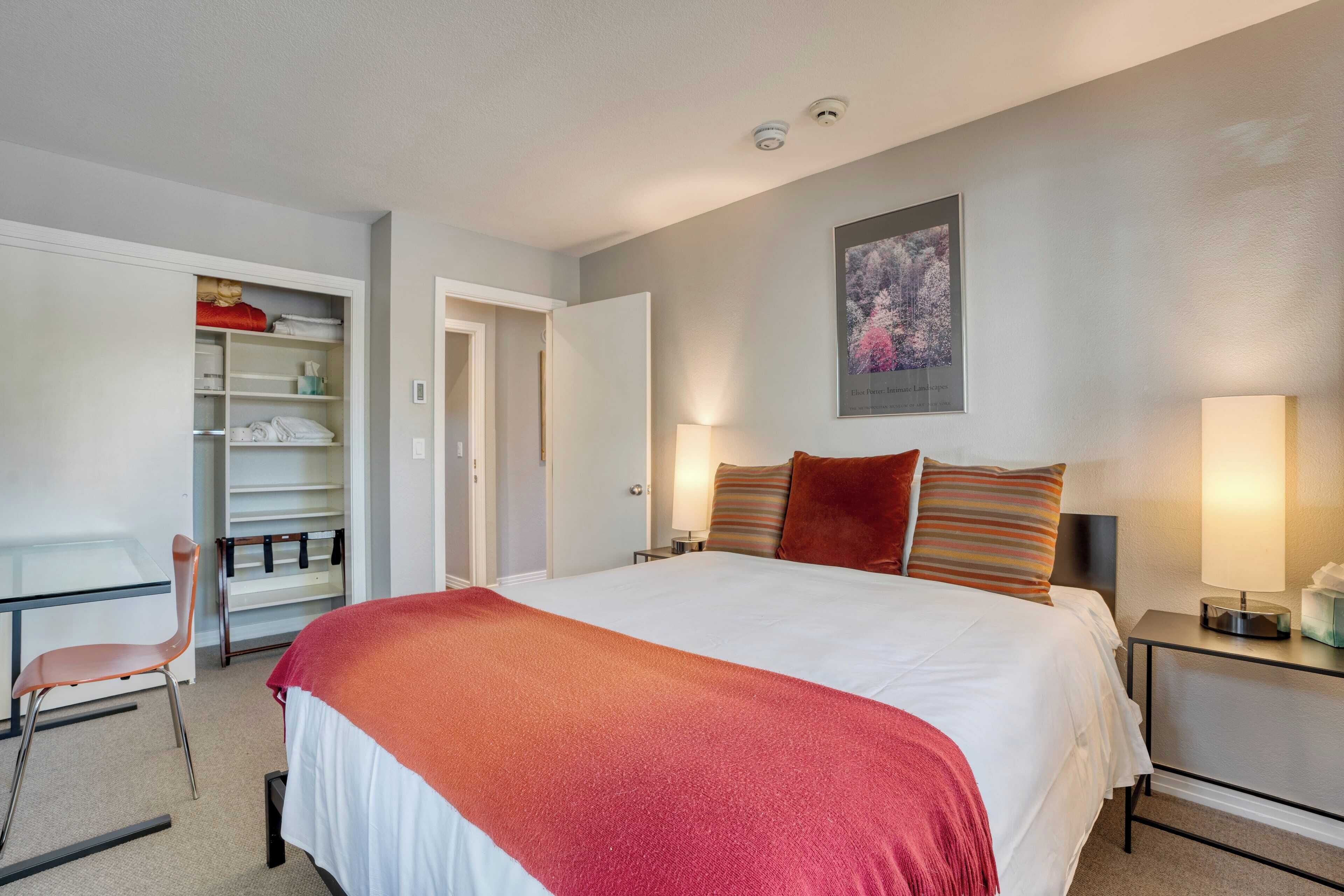 Habitación de hotel con una cama grande, un escritorio con una silla, un armario y dos lámparas de noche.