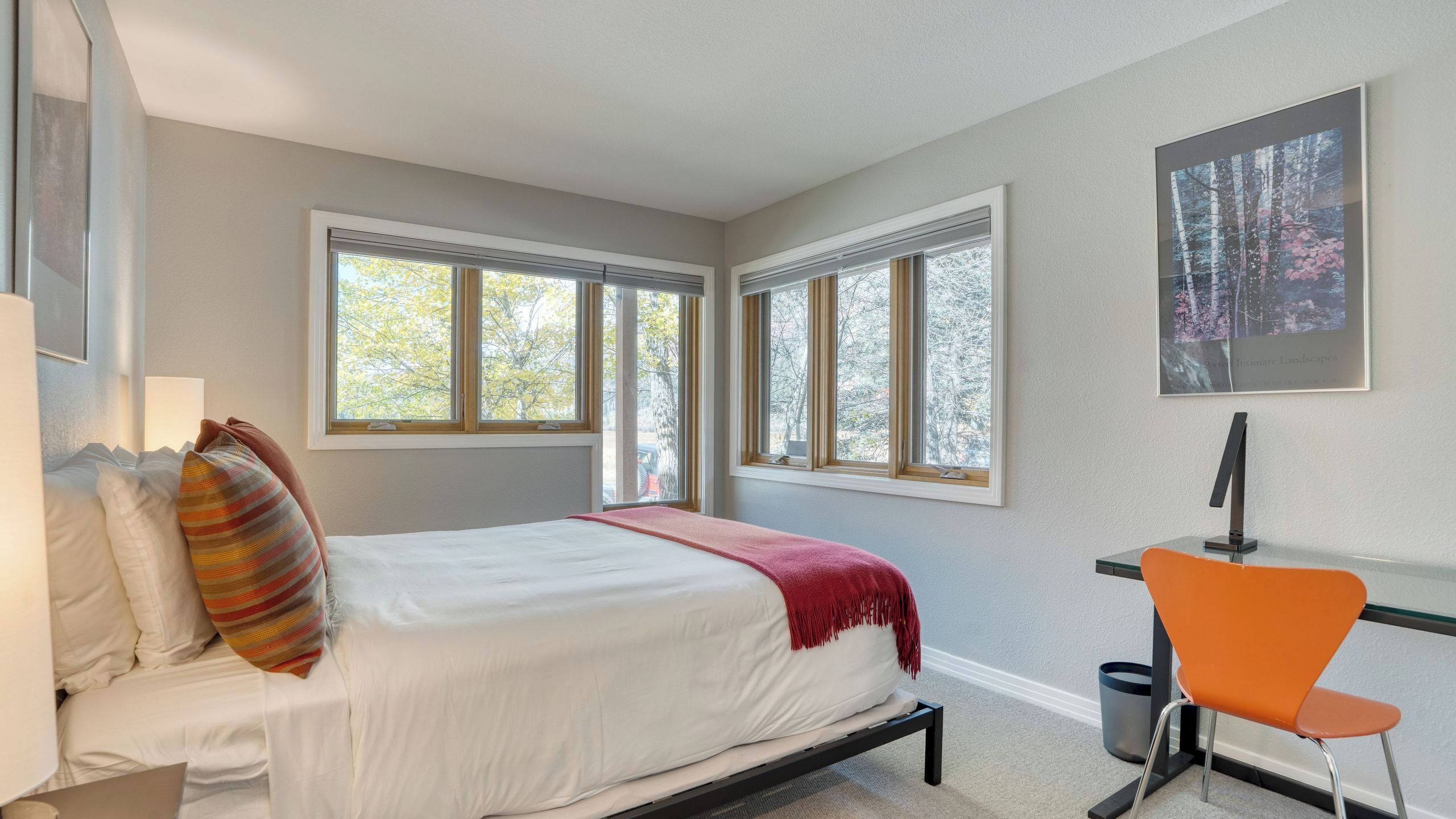 Un dormitorio con cama, dos ventanas, un escritorio y una silla.