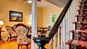 A staircase with a handrail, a dining area with chairs and a table, and a painting on the wall.