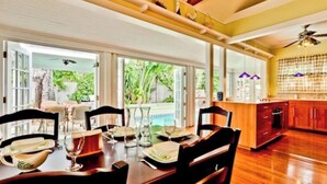 A dining area with a pool view, wooden flooring, and a kitchen with a view.