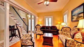 A spacious living room with a wooden floor, a sofa set, a coffee table, and a ceiling fan.