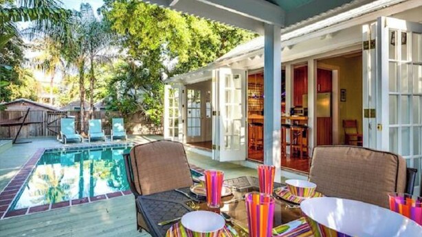 A pool area with lounge chairs, a table with striped napkins, and a covered patio with a view of the pool.