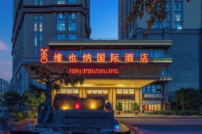 Hotel Vienna International, con un llamativo letrero de neón, una fuente de piedra y una entrada bien iluminada.