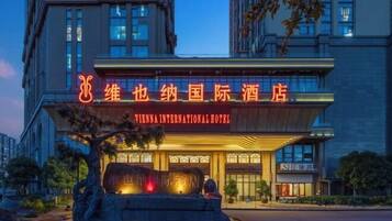 The Vienna International Hotel with a prominent neon sign, a stone fountain, and a well-lit entrance.