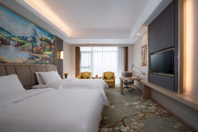 A hotel room with two beds, a desk, a chair, a television, and a large painting on the wall.