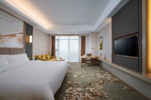 Habitación de hotel con cama, escritorio, silla, televisor y obras de arte en la pared.