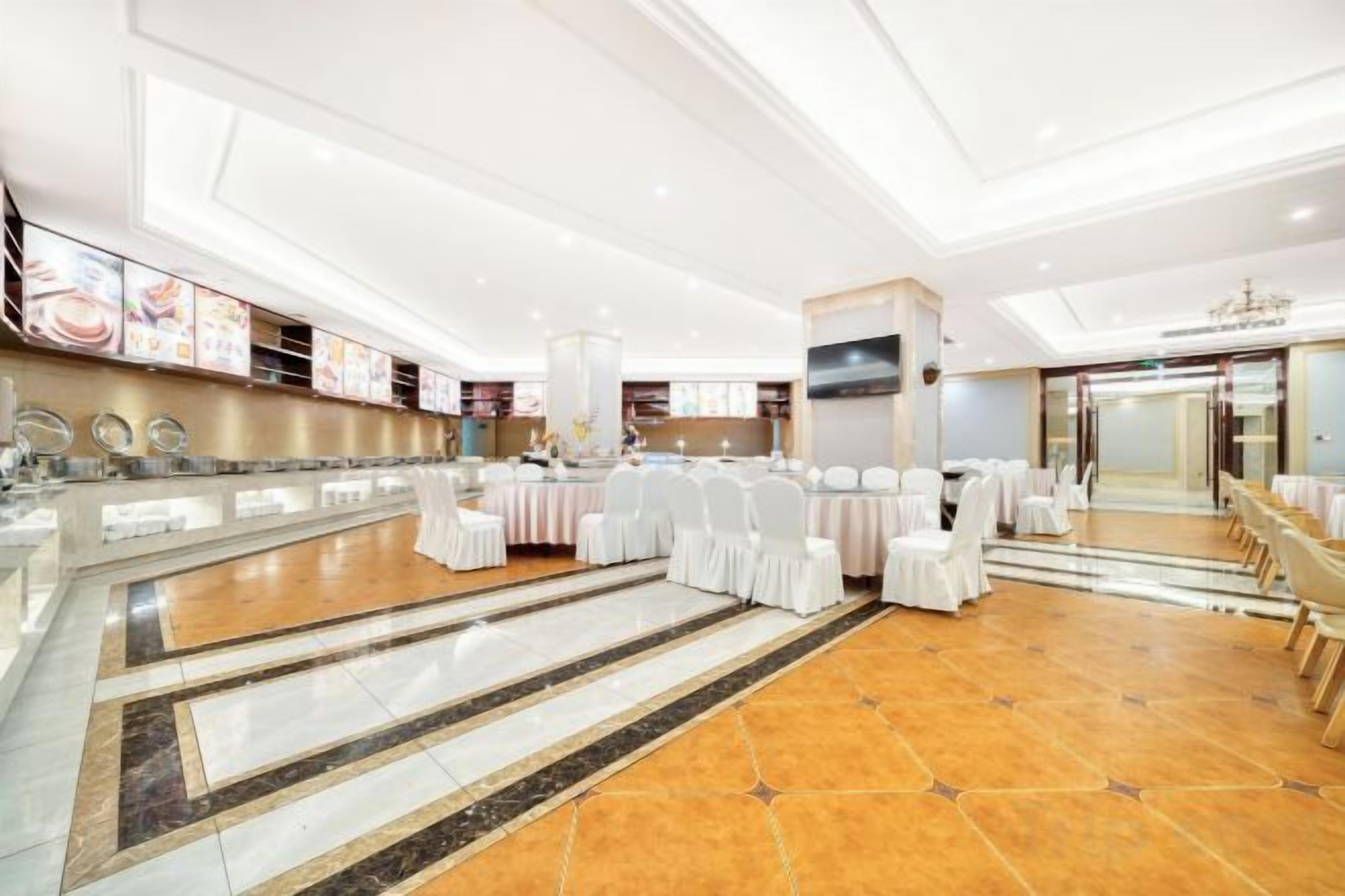 Un amplio salón de banquetes con una larga mesa dispuesta para eventos, un espejo grande y una moderna lámpara de araña.