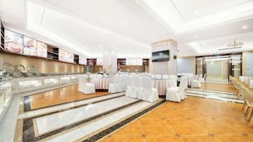 Un amplio salón de banquetes con una larga mesa dispuesta para eventos, un espejo grande y una moderna lámpara de araña.