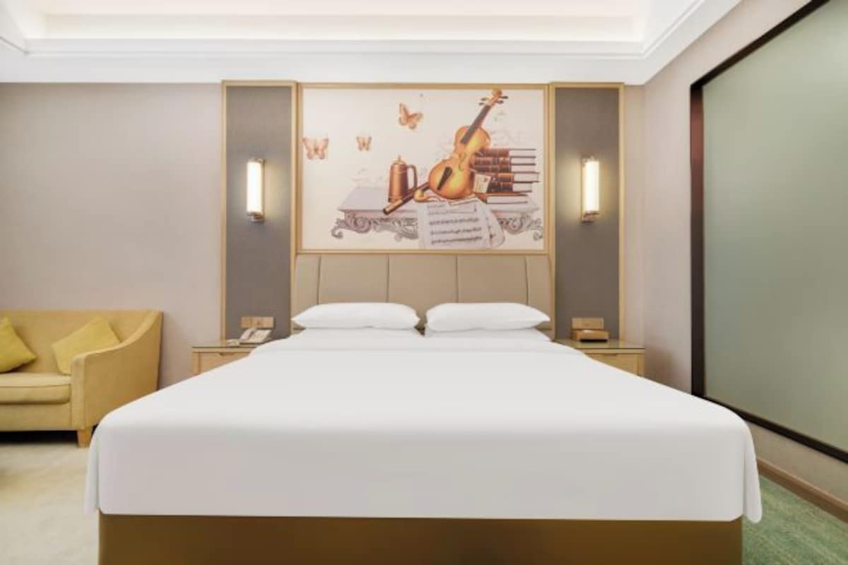 Habitación de hotel con cama, un cuadro de un violín, dos lámparas de noche, una mesita de noche y un sofá.