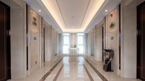 A hotel corridor with a polished marble floor, a central table with a vase, and doors on either side.