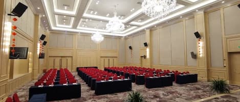 A conference room with rows of chairs, a chandelier, and a floral carpet.