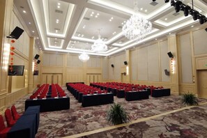 Une salle de conférence avec des rangées de chaises, un lustre et une moquette à motifs floraux.